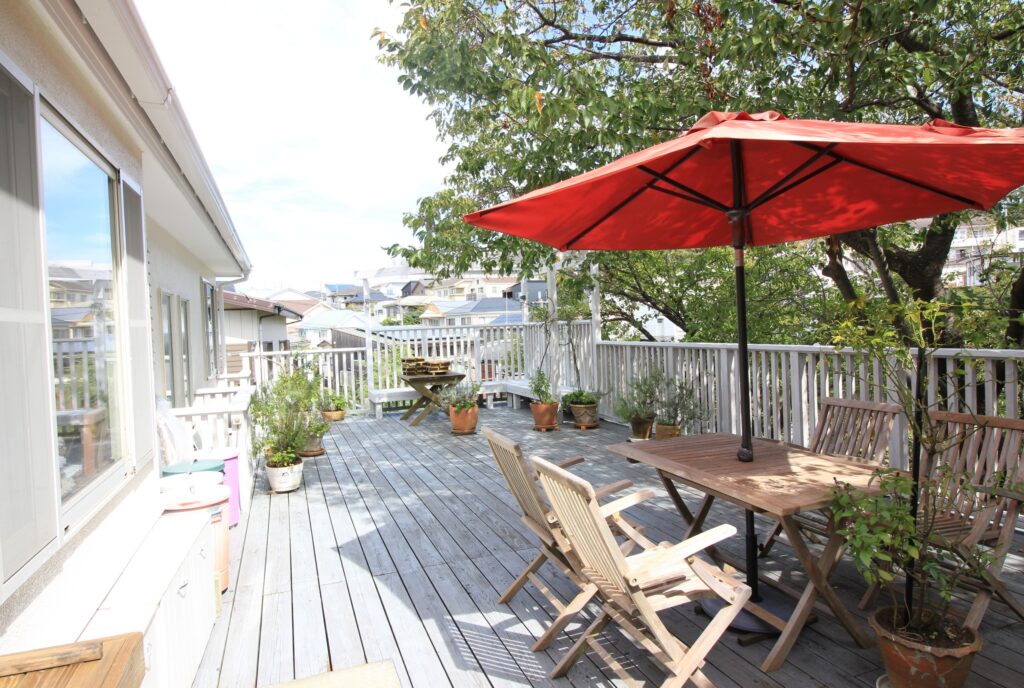 白い傾斜地ウッドデッキに赤いパラソル　長持ちするデッキ