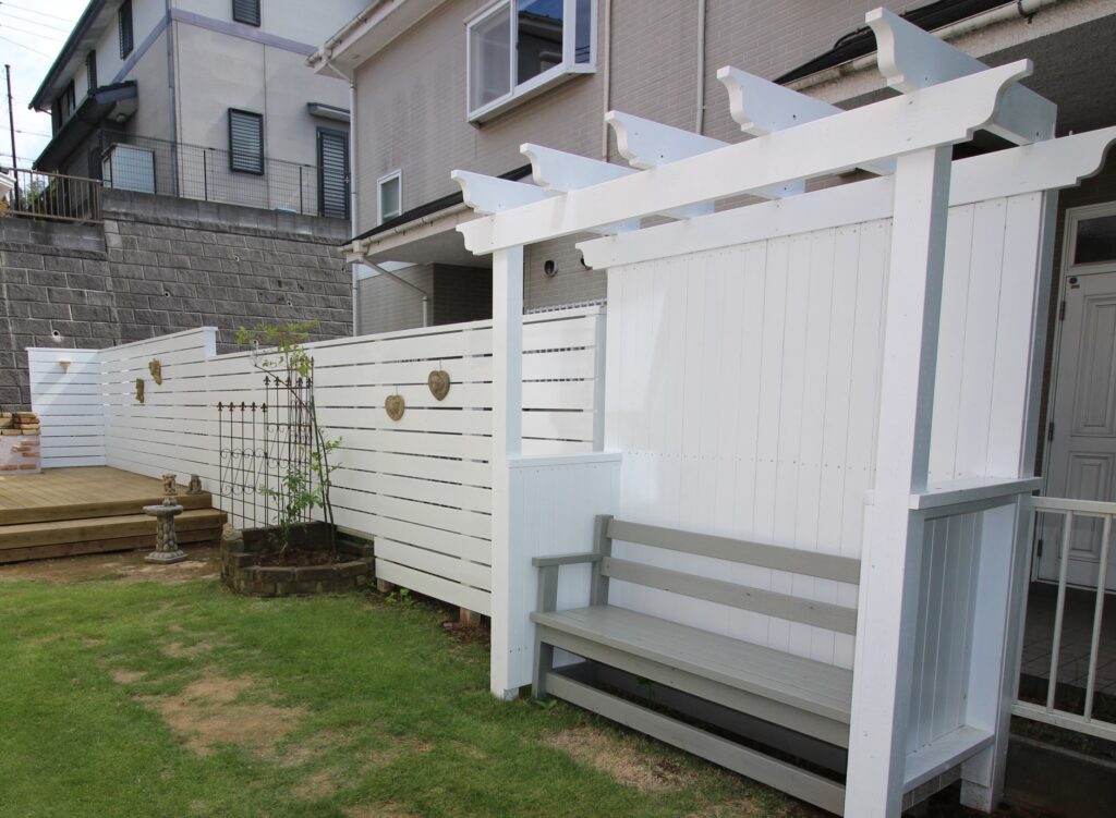 白い木製フェンスと木製パーゴラ、無塗装でもOKな国産杉加圧注入のデッキ、グレーのベンチ