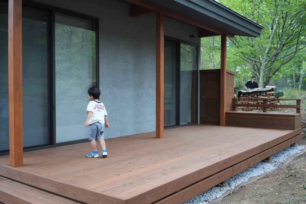 塗装したウッドデッキを歩く男の子と薪の世話をしているお父さん