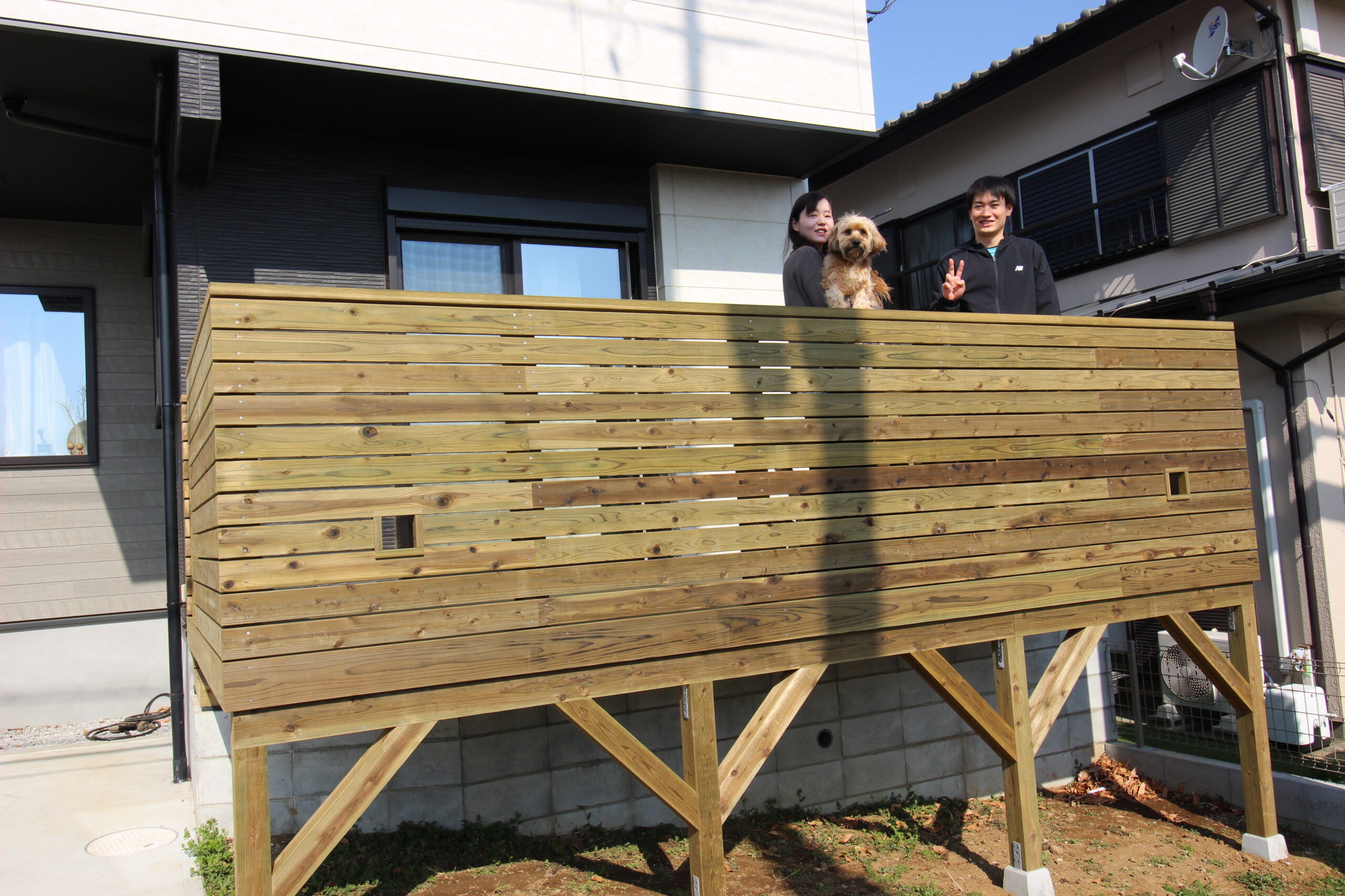 犬を抱っこして笑顔のご夫婦 新しく家に作った天然木のウッドデッキ 小窓はワンちゃん用